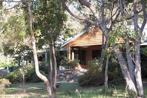 A wooden house with a brick exterior, surrounded by trees and a grassy yard. - Vaila—Bushland Charm near Beaches & Top Wineries (Yallingup)