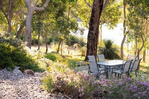 An outdoor dining area with a table and chairs, surrounded by trees and plants. - Vaila—Bushland Charm near Beaches & Top Wineries (Yallingup)