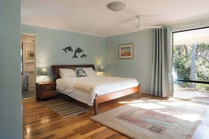 A bedroom with a bed, nightstands, a window with curtains, and a view of trees.