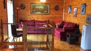 L’intérieur d’un chalet en bois, avec un escalier en bois, un canapé violet, une table à manger et un réfrigérateur.