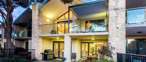 Un edificio de dos pisos con balcón, zona de barbacoa y jardín bien cuidado.