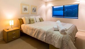 A bedroom with a bed, a nightstand, a lamp, a window with a view, and two framed pictures on the wall. - Surfside 9: In the Idyllic Yallingup Beach Scene (Yallingup)