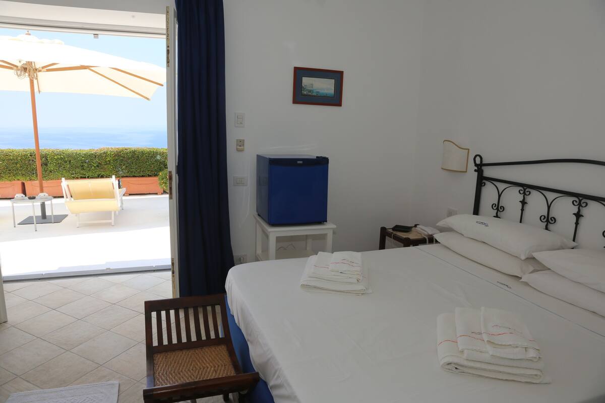 A hotel room with a bed, a TV, a small table, and a view of the outdoors.