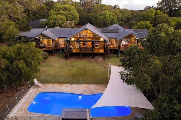 A two-story house with a swimming pool, surrounded by trees.