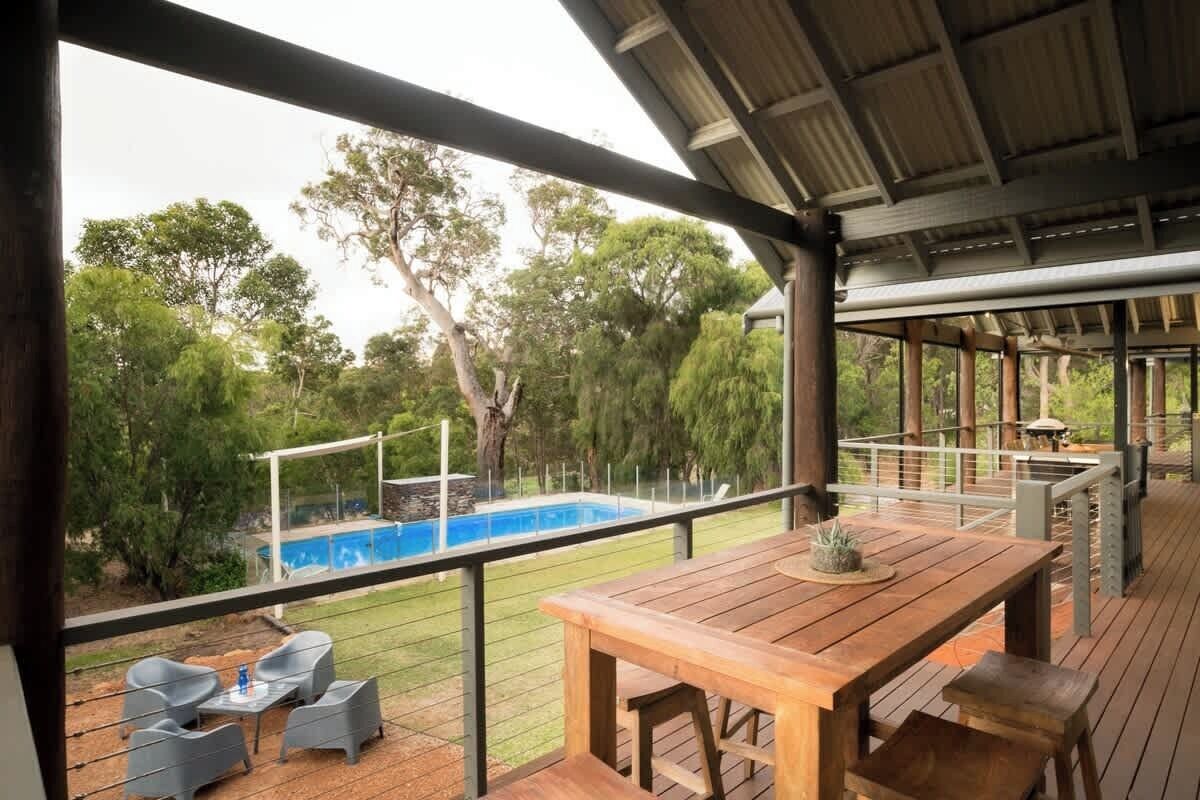 A wooden deck with a table and chairs, overlooking a swimming pool and lush greenery.