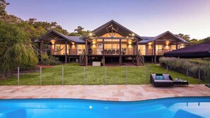 A modern two-story house with a swimming pool, outdoor seating, and a well-maintained lawn.