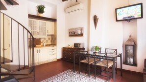 Un comedor con mesa y sillas, una cocina al fondo, una escalera y un televisor montado.