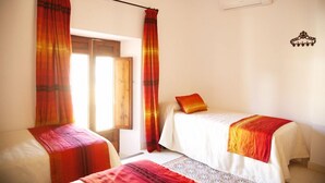 Una habitación con dos camas, cada una con una manta roja y blanca, una ventana con cortinas y un aire acondicionado de pared.