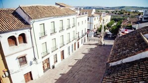 A cobblestone street lined with white buildings with terracotta roofs, balconies, and a clear view of the surrounding landscape.