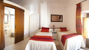A bedroom with two beds, a nightstand, a wardrobe, and a bathroom visible through an open door.