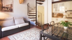 Una sala de estar moderna con un sofá, una mesa de comedor de vidrio y una escalera espiral que lleva a una cocina.