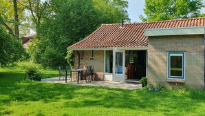 Una petita casa de maó amb teulada de rajola, un pati amb taula i cadires, i una zona de jardí.