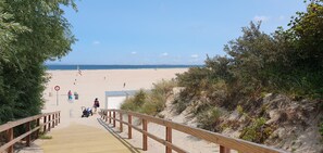 A wooden boardwalk leading to a sandy beach with a clear sky and wind turbines in the distance. - Philene, cottage in Zeeland at 5 minutes walk from te beach. (Vrouwenpolder)