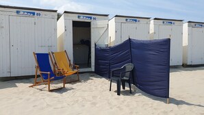 Fila de cabanes de platja blanques, numerades del 89 al 95, amb una cadira de platja blava i una cadira de plàstic negra al davant.