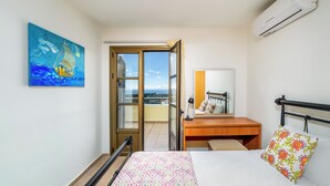 A bedroom with a bed, a desk, a chair, a window, and a painting. - Aegean Blue Villas - Aphrodite Villa (Kalathos)