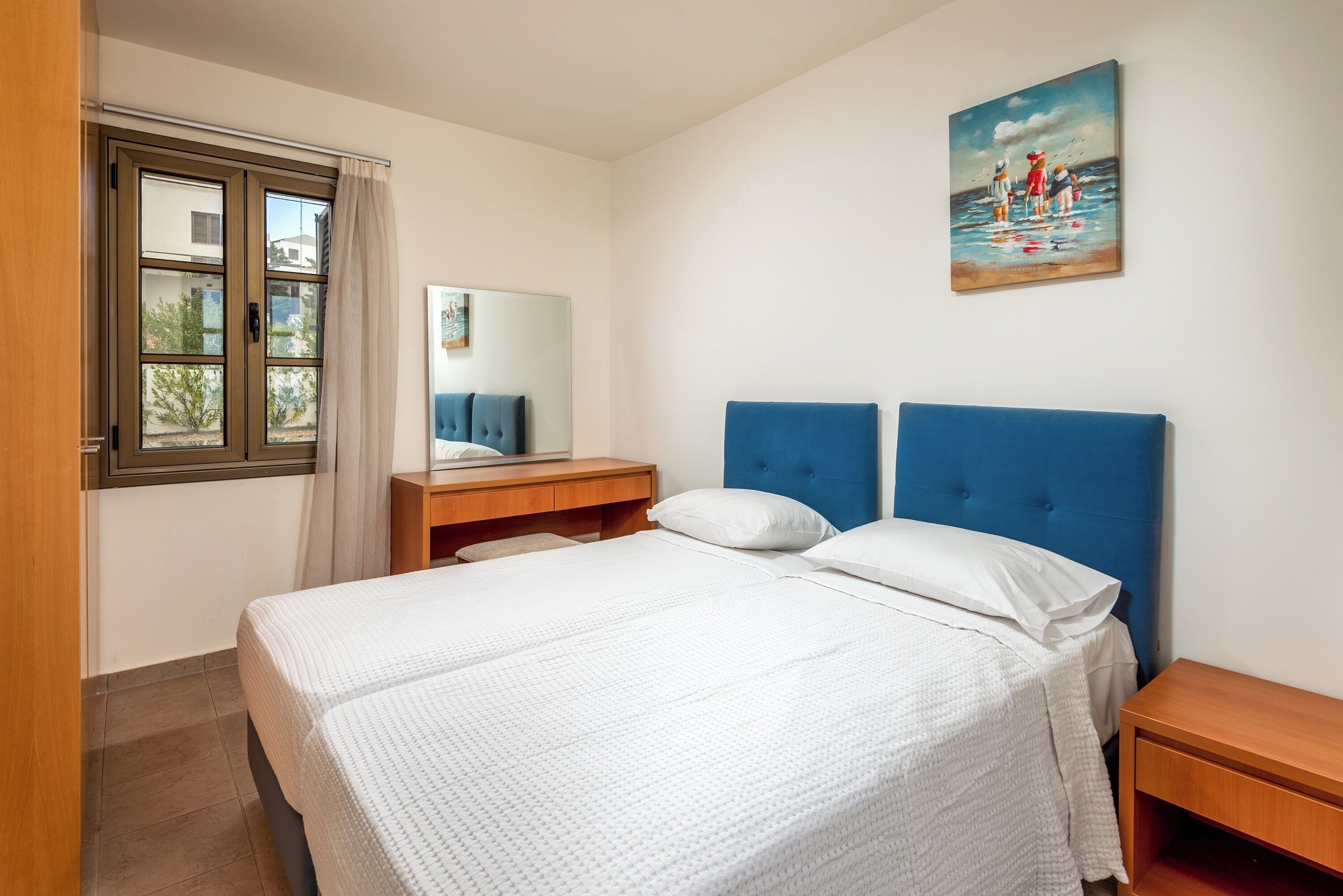 A bedroom with a bed, a nightstand, a mirror, a painting, and a window with curtains.
