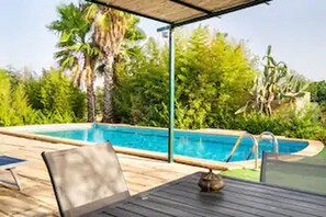 Un espace aménagé au bord de la piscine, comprenant un coin salon couvert et une piscine.