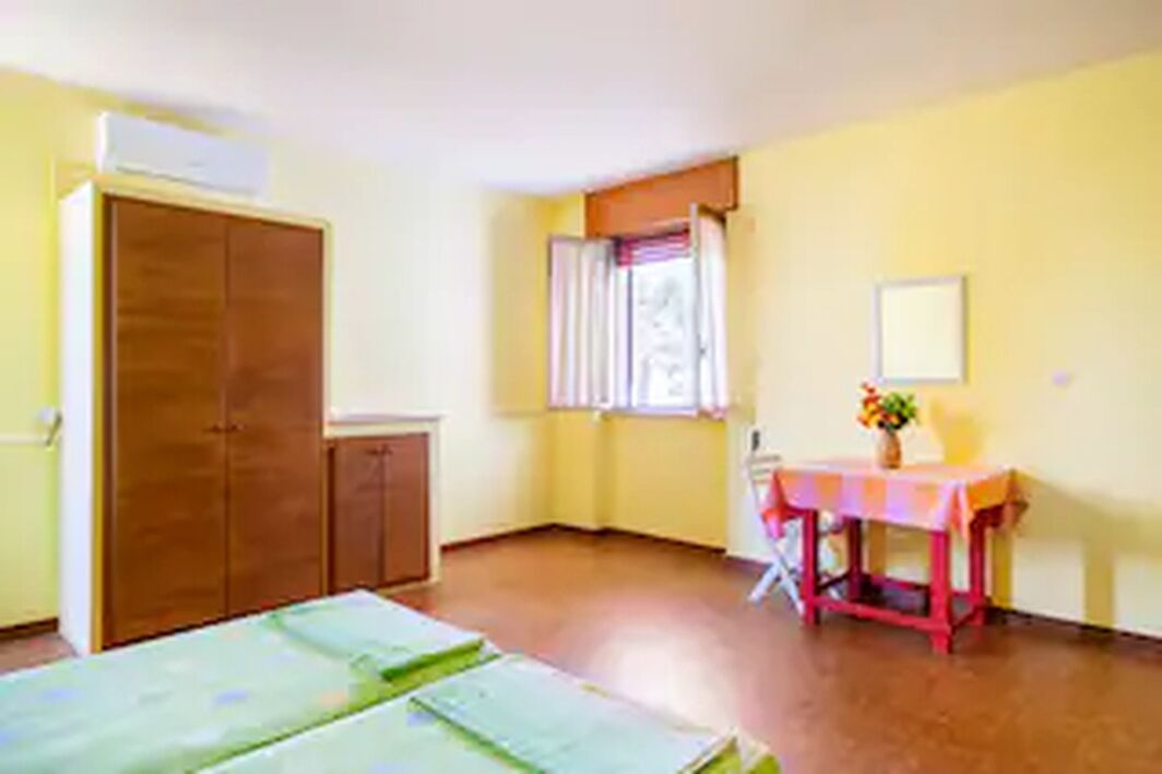 A room with a bed, a table with a vase, a window with curtains, and a wardrobe.