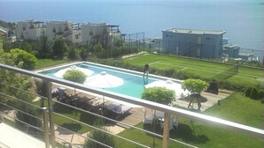 Zona de piscina amb gandules i ombrel·les, envoltada de vegetació i edificis.