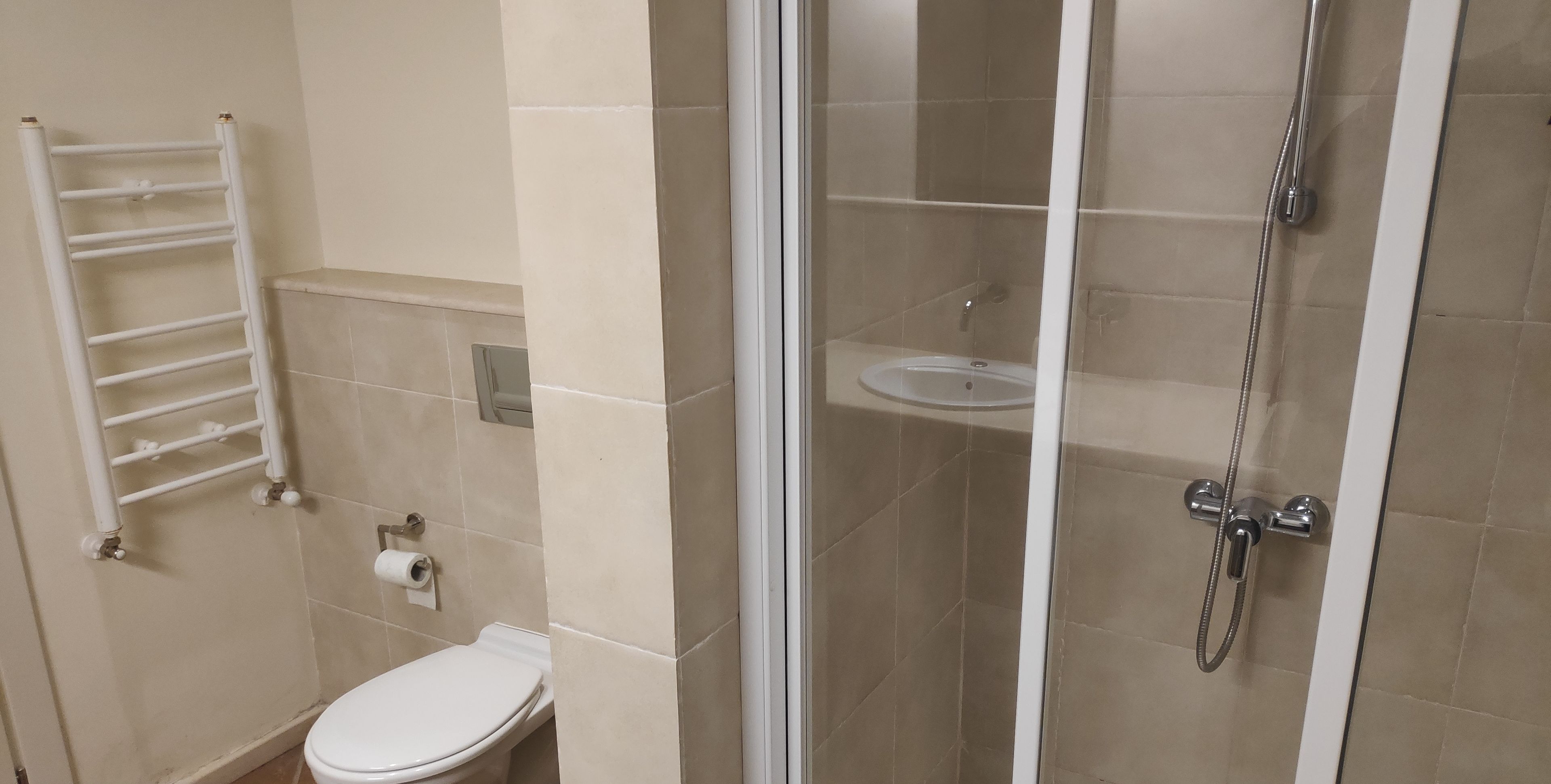 A bathroom with a toilet, a white towel rack, a shower enclosure, and a toilet paper roll.