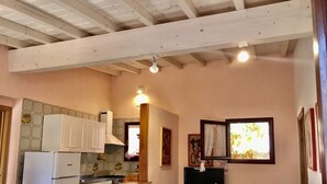 A kitchen with white cabinets, a stove, and a tiled backsplash. There are two ceiling lights and a window with a view of greenery. - Silvia A/B - SILVIA B (Capoliveri)