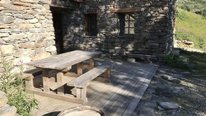 Ein rustikales Steinhaus mit einer Holzdiele, einem Picknicktisch und einem Fass.