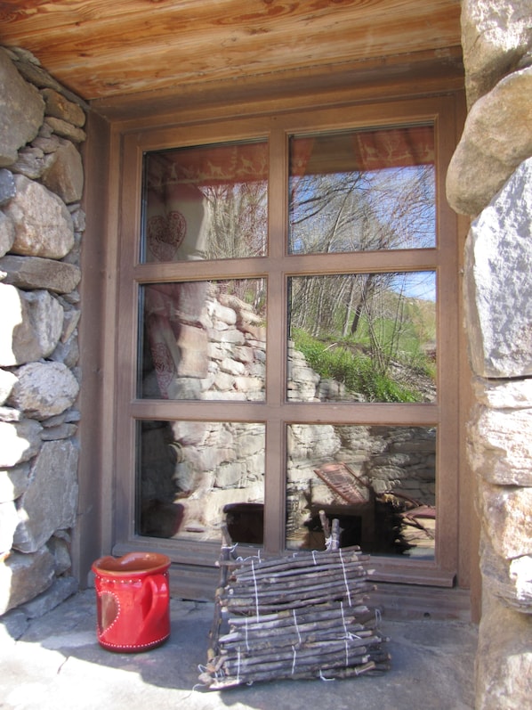 A stone building with a large window, a red pot, and a stack of wooden planks outside.