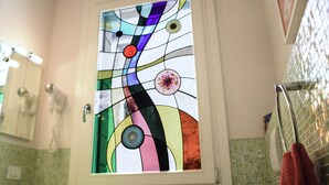 Ein Badezimmer mit einer farbenfrohen Glas-Tür, einer grün gefliesten Wand und einem Handtuchhalter.