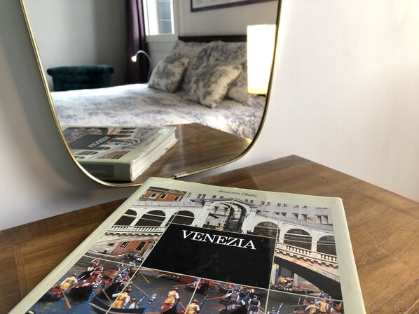 A brochure titled "Venezia" on a wooden table, reflecting a room with a bed and a window.