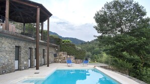 A pool with two blue chairs, a stone building, and a covered area with a railing. - Historic village house with private pool, gardens & outdoor dining, near Bagnone (Bagnone Massa Carrara)