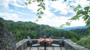 Un patio in pietra con tavolo e sedie, con vista su una valle boscosa.