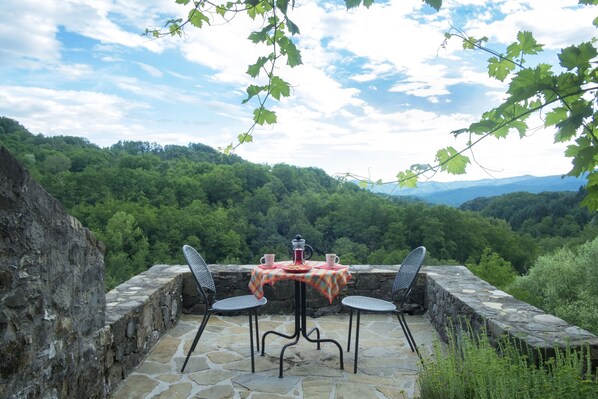Une terrasse en pierre avec une table et des chaises, donnant sur une vallée boisée.