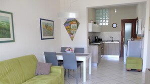 A living room with a green sofa, a dining table with chairs, a kitchen area with a sink and stove, and a small green stool. - apartment under the hill of San Miniato (san miniato)