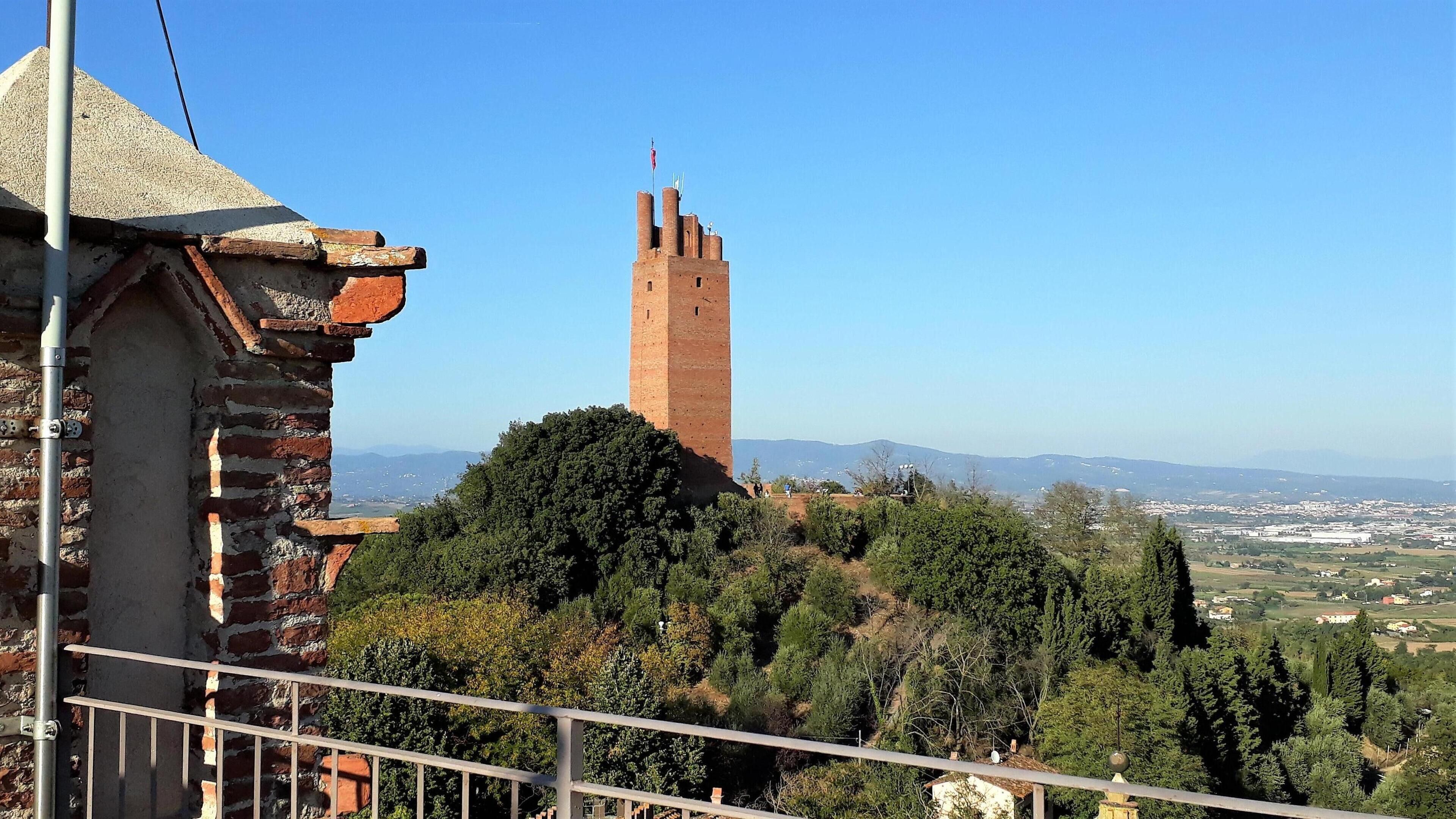 Una torre storica con una vista chiara del paesaggio circostante, inclusi montagne lontane e un paese.