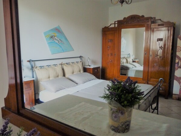 A bedroom with a bed, a wooden wardrobe, a mirror, and a painting on the wall.