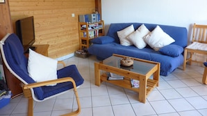 Una sala de estar acogedora con un sofá azul, una mesa de centro de madera y una estantería.