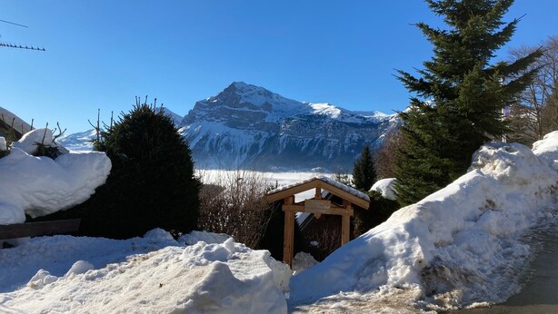 Paisaje nevado con una montaña al fondo, una estructura de madera y montones de nieve.