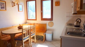 Una cocina funcional con una mesa y sillas de madera, dos ventanas, un lavamanos y un hervidor.