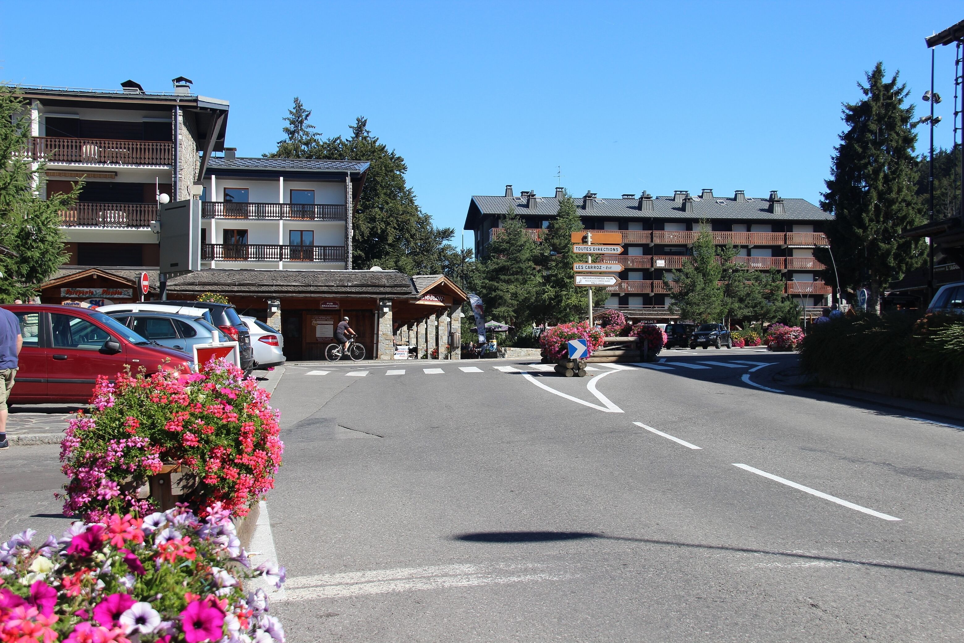 Une rue bordée de voitures garées, un cycliste et des immeubles dotés de balcons.