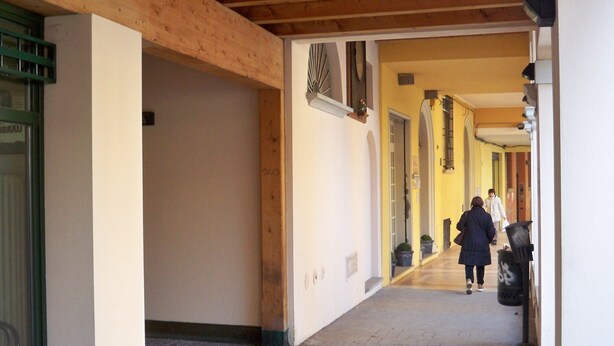 A corridor with wooden beams, a tiled floor, and a person walking away.
