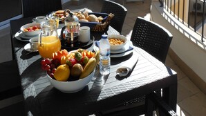 Ein Balkon mit Esstisch, gedeckt mit Frühstücksartikeln, darunter Obst, Brot und Getränke.