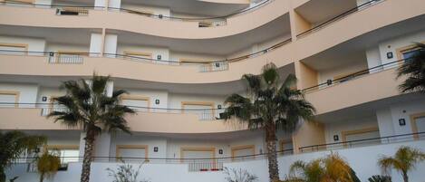 Un edificio de varios pisos con balcones, palmeras y un cielo despejado.