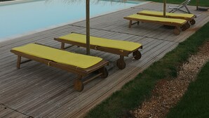 Ein Poolbereich mit Holzdeck, gelben Liegestühlen und Strohschirmen.