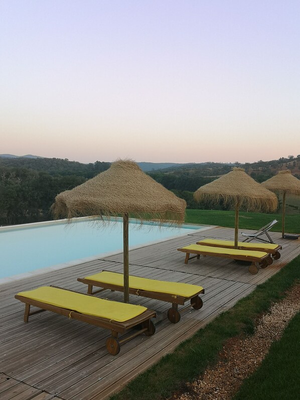 A poolside area with wooden deck, yellow lounge chairs, and straw umbrellas.