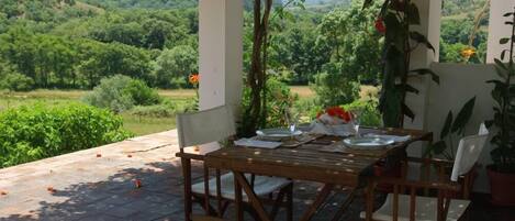 An outdoor dining area with a table and chairs, surrounded by a view of a lush green landscape.
