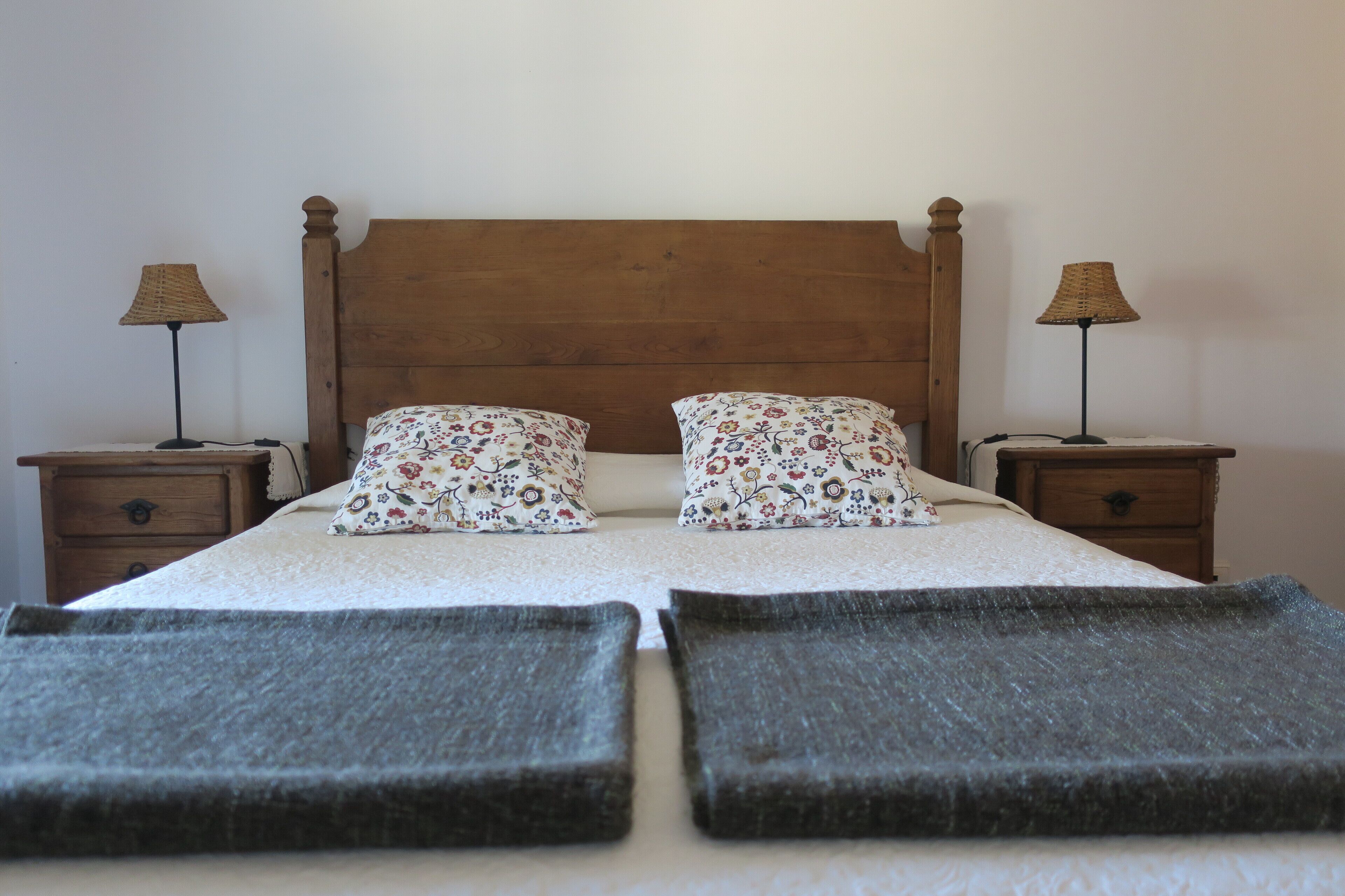 Un letto matrimoniale con cuscini floreali, due comodini con lampade e un poggiatesta in legno.