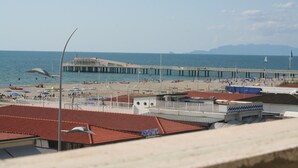 Vista costeira com um cais que se estende para o mar, guarda-sóis na praia e um céu limpo.