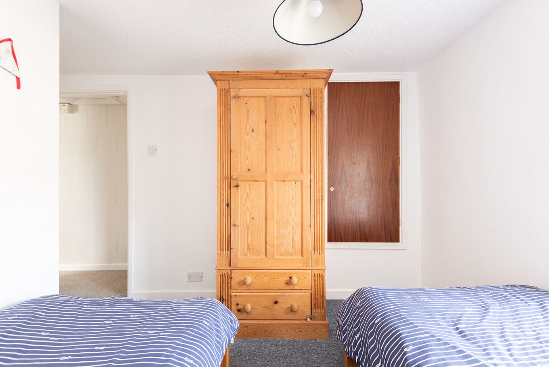 A bedroom with two beds, a wooden wardrobe, and a wooden door.