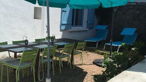 Un patio al aire libre con una mesa, sillas, un paraguas grande y un muro de piedra.