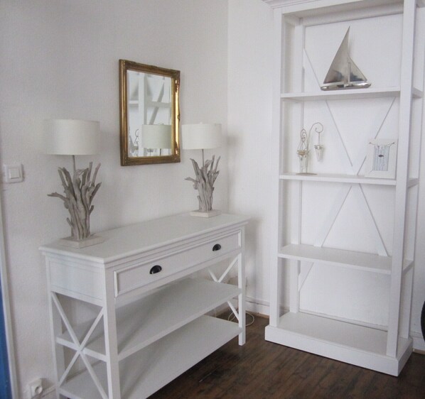 A white console table with two lamps and a mirror, flanked by a white shelving unit with decorative items.